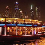 Colorful Dubai night city skyline with illuminated boat cruise on water.
